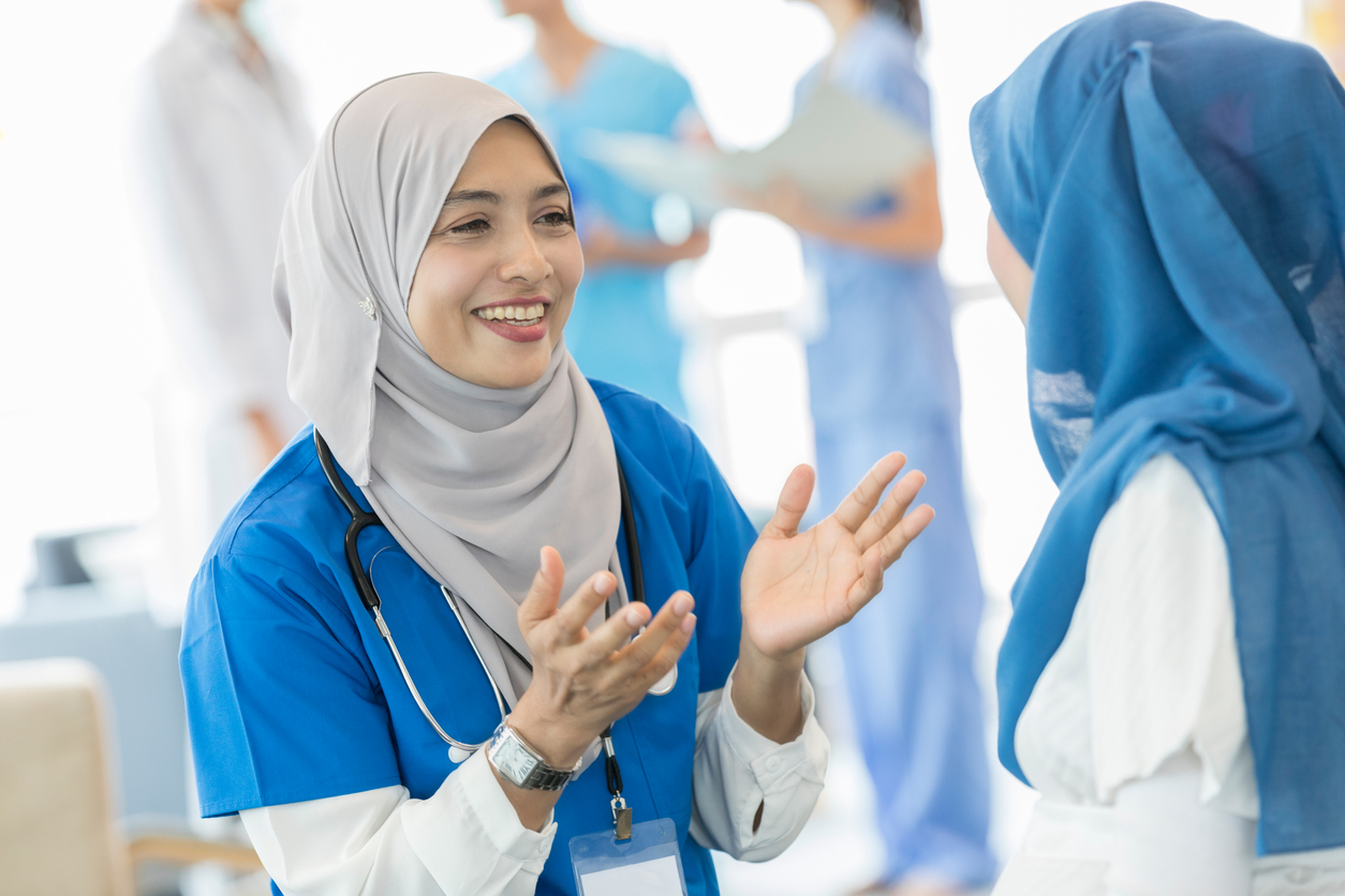 Cheerful female nurse gestures as she talks with a pregnant patient.
